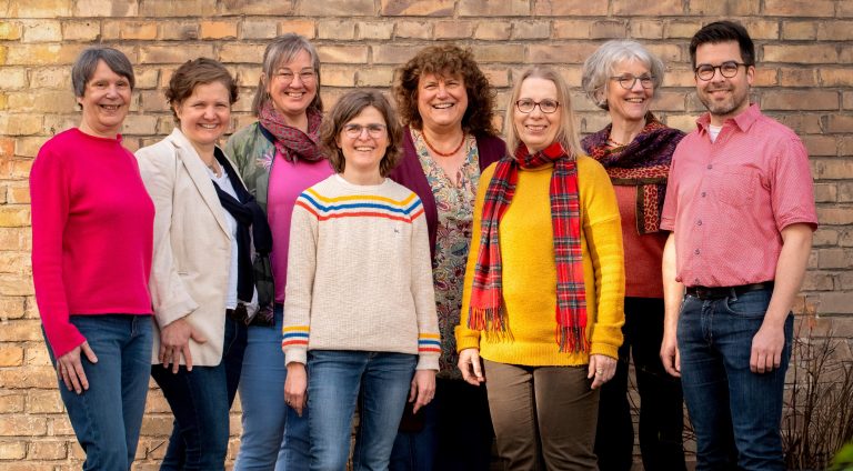 Zu sehen ist das Redaktionsteam der gesundheitspress. Sieben Frauen und ein Mann stehen vor einer Backsteinwand und lächeln in die Kamera.